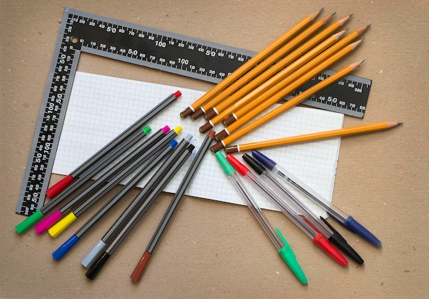 Matite e penne colorate con blocco note in bianco e righello di metallo su sfondo di cartone