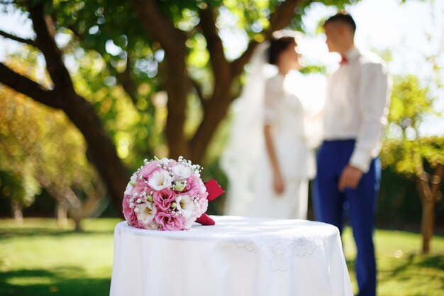 Matrimonio bouquet da sposa con fiori rosa e bianchi sul tavolo in giardino sullo sfondo della sposa e dello sposo. Concetto di matrimonio