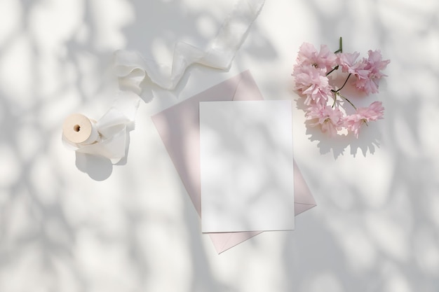 Matrimonio natura morta Mockup di cancelleria primavera femminile Rosa ciliegio giapponese sakura fiori alla luce del sole Invito biglietto di auguri vuoto Busta rosa cipria Sfondo tavolo screziato bianco