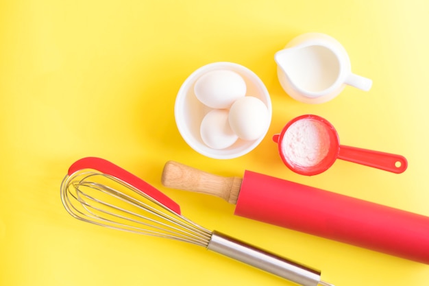 Mattarello, frusta, uova, latte su uno sfondo giallo, vista dall'alto. Il concetto di impasto.