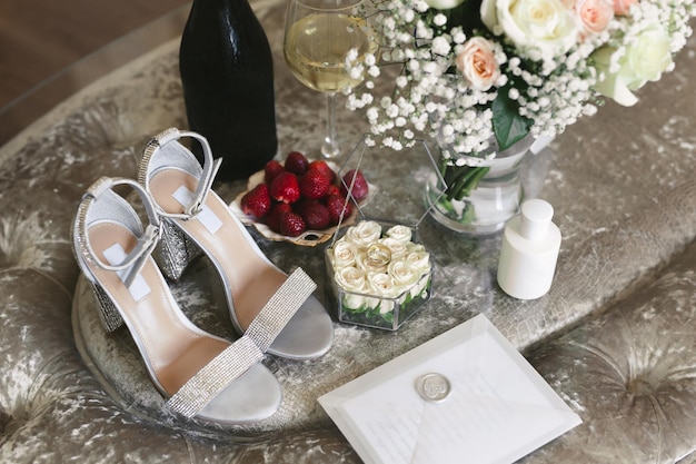 Mattina della sposa il giorno del matrimonio: scarpe, anelli, champagne, fragole e un bouquet.