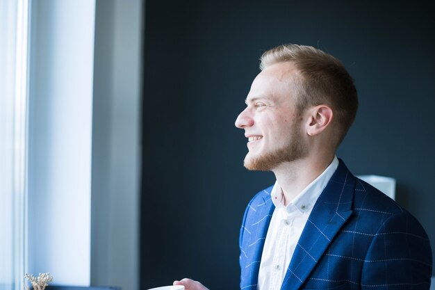 mattina di sole un giovane uomo d'affari beve caffè in un ufficio uomo europeo con una giacca blu