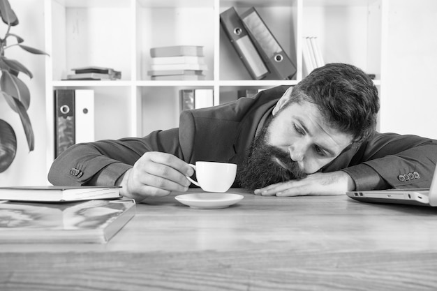 Mattina dura Abito formale hipster barbuto rilassante con caffè Vita in ufficio Primo caffè Notte insonne La procrastinazione è ladro del tempo Uomo bello capo dormire in ufficio a bere caffè