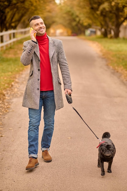 Mattinata al parco. Uomo che fa una passeggiata mattutina con un cane e parla al telefono