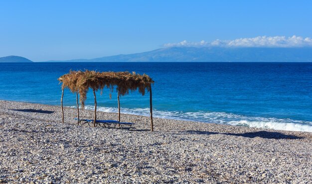 Mattinata estiva spiaggia di ciottoli con lettini e baldacchino (Borsh, Albania).