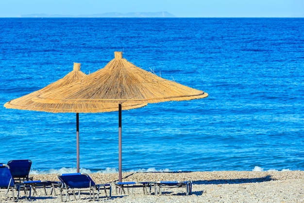 Mattinata estiva spiaggia di ciottoli con lettini e ombrelloni di paglia (Borsh, Albania).