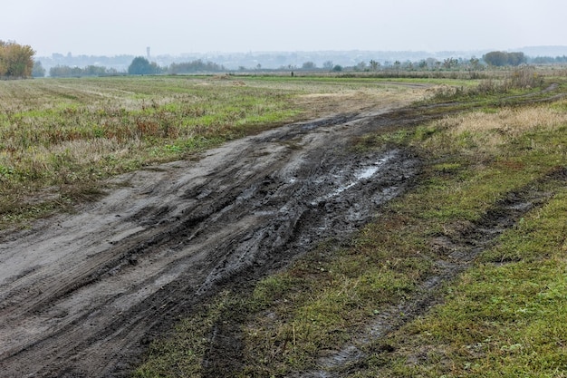 Mattinata nebbiosa autunnale paesaggio rustico con strada sterrata in primo piano e piccoli edifici sulla collina sullo sfondo