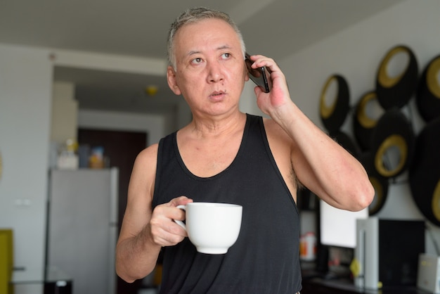 Maturi il caffè giapponese della tenuta dell'uomo mentre parlano al telefono a casa