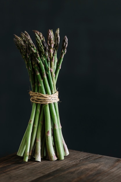 Mazzetto di asparagi freschi crudi sul tavolo di legno su sfondo nero.