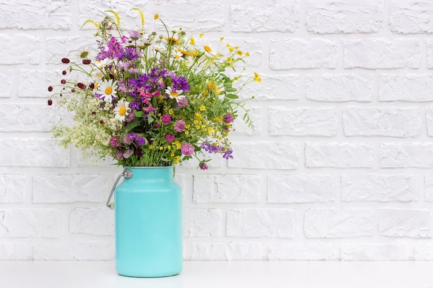 Mazzo dei fiori luminosi in vaso del barattolo di latta sul muro di mattoni bianco del fondo. Modello per cartolina. Concetto Festa della donna, Festa della mamma, Ciao estate o Ciao primavera.