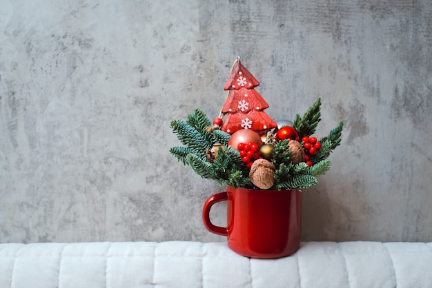 Mazzo dei rami dell'abete in una tazza rossa e nei giocattoli di Natale su un fondo concreto.