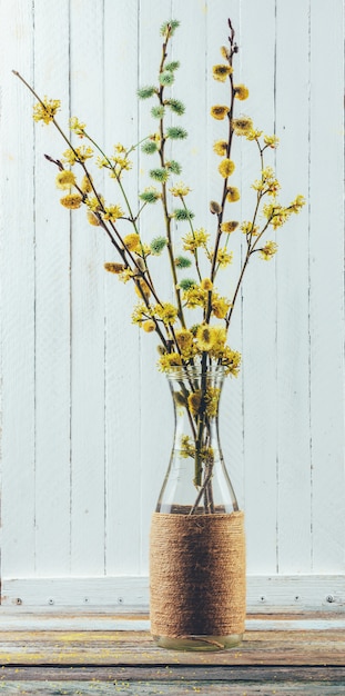 Mazzo dei rami di fioritura del salice e del corniolo in un vaso sulla tavola su un fondo di legno bianco
