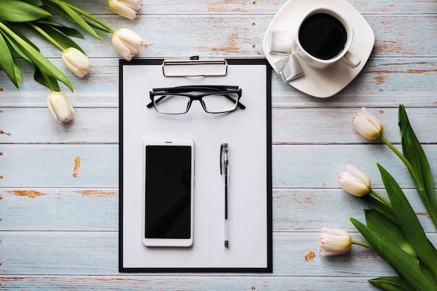 Mazzo dei tulipani bianchi con uno smartphone, una tazza di caffè e una compressa di carta su una tavola di legno