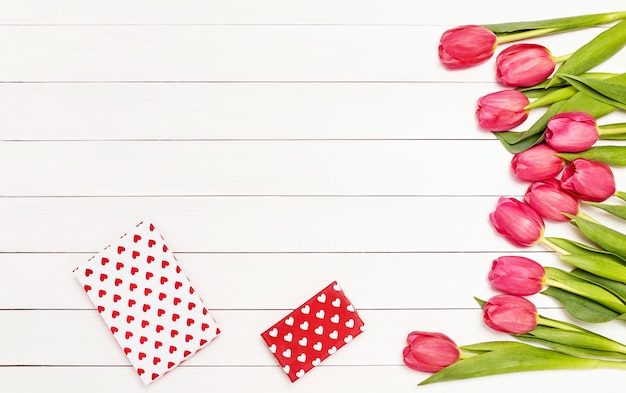 Mazzo dei tulipani rosa sulla tavola di legno bianca decorata con i contenitori di regalo.