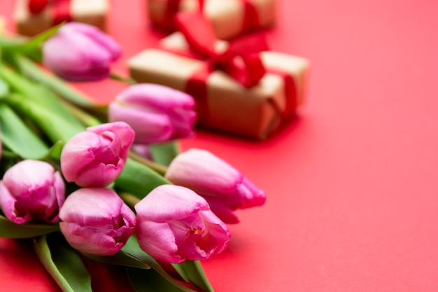 Mazzo del fiore del tulipano e contenitori di regalo rosa su fondo rosso. San Valentino