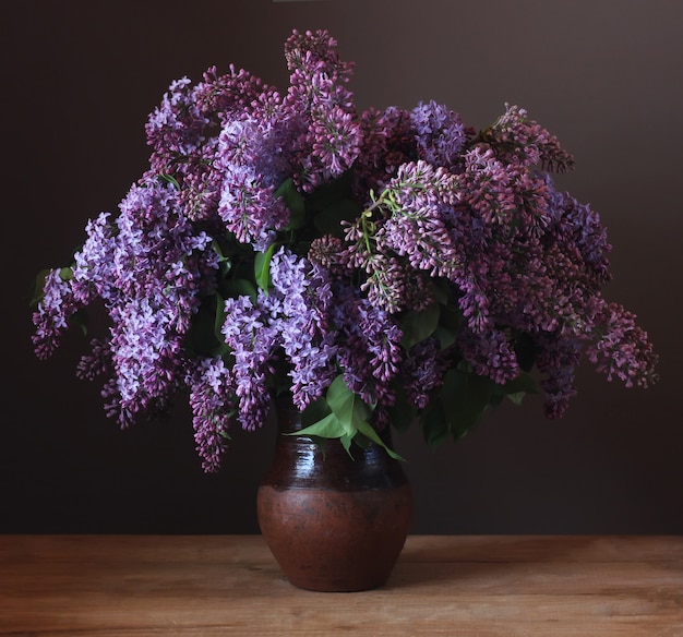 Mazzo del lillà porpora in una brocca dell'argilla sulla tavola. Natura morta con fiori.