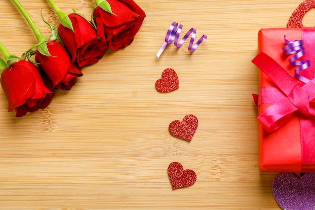 Mazzo della rosa rossa e contenitore di regalo sul bordo di legno. Concetto di San Valentino
