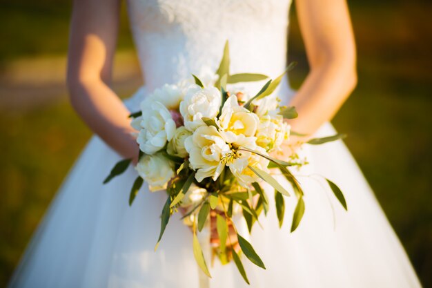 Mazzo delle rose dei fiori di nozze in mani della sposa con il vestito bianco su fondo