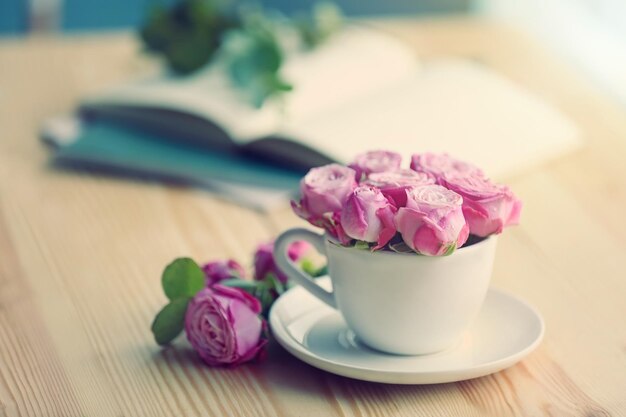 Mazzo delle rose fresche in tazza sulla tavola di legno