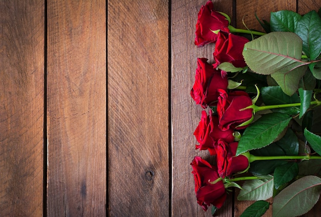 Mazzo delle rose rosse sul fondo di legno della tavola