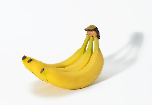 Mazzo di banane mature gialle in buccia su un fondo bianco, fine su