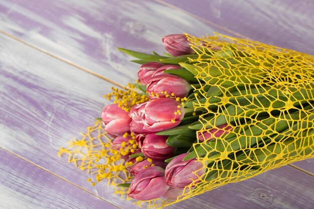 Mazzo di bei tulipani rosa e fiori di mimosa su una superficie di legno viola. Avvicinamento