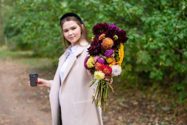 Mazzo di fiori autunnali e una tazza di tè nelle mani di una ragazza carina