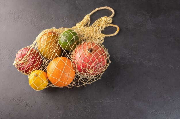 Mazzo di frutta, verdura e verdure organiche miste in un sacchetto di stringa su sfondo scuro.