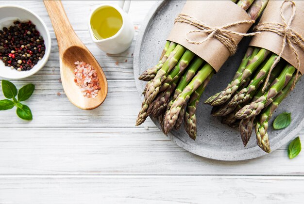 Mazzo di gambi di asparagi crudi con diverse spezie e ingredienti su una superficie di legno