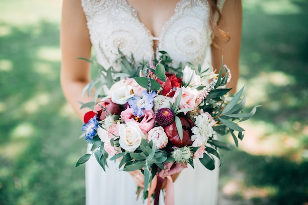 Mazzo di nozze dei fiori tenuto dal primo piano della sposa. Sfondo verde