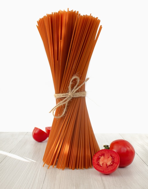 Mazzo di pasta rossa italiana cruda con pomodori su sfondo chiaro