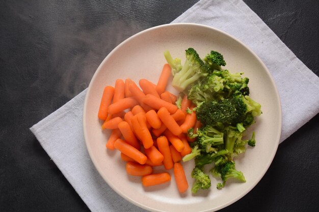 Mazzo di piccole carote bollite e broccoli cotti sul piatto bianco Mangiare sano