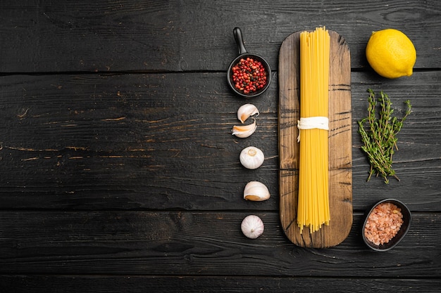 Mazzo di spaghetti, set di pasta cruda, su sfondo di tavolo in legno nero, vista dall'alto piatta, con spazio di copia per il testo