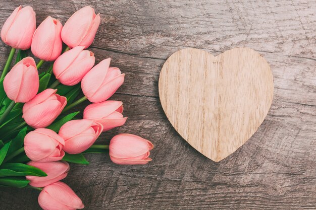 Mazzo di tulipani rosa e un biglietto di S. Valentino a forma di cuore da legno, su un fondo di legno