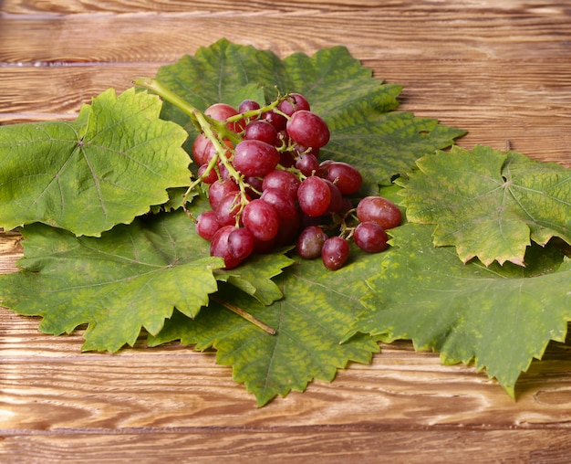 Mazzo di uva con le foglie verdi su una tavola di legno