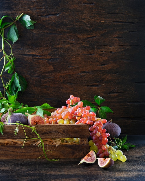Mazzo maturo di uva rossa e verde e vino bianco in un decantatore sui bordi di legno anziani