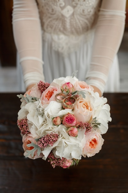Mazzo nuziale delle peonie e delle rose bianche con il primo piano delle fedi nuziali. La sposa tiene fedi nuziali e bouquet da sposa.