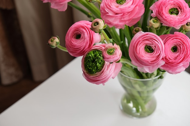 Mazzo rosa del ranunculus in vaso di vetro trasparente sulla tavola bianca.