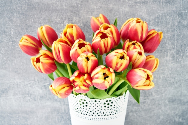Mazzo rosso dei tulipani in vaso di fiori bianco sullo spazio grigio della copia del fondo di festa del fondo