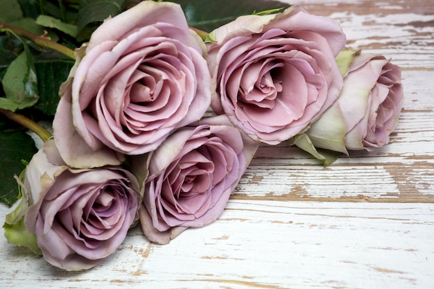 Mazzo viola delle rose e cartolina d'auguri in bianco sopra la tabella di legno.