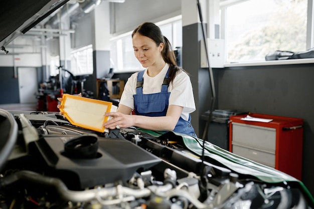 Meccanica automobilistica femminile che cambia il filtro dell'aria del motore in auto