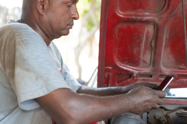 Meccanico africano che controlla il suo telefono nel suo negozio di riparazioni auto