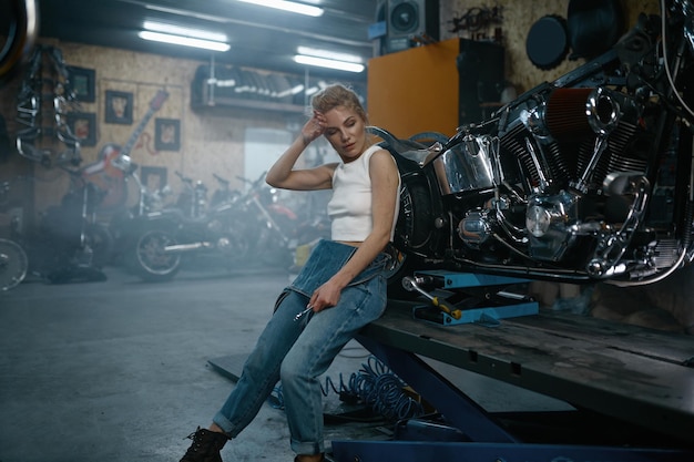 Meccanico attraente della donna che posa per la macchina fotografica al garage del motociclo. Donna di riparazione professionale in officina autentica