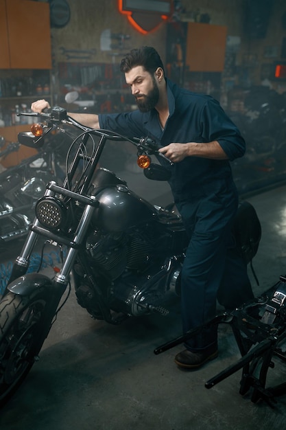 Meccanico automatico che spinge la motocicletta sul cavalletto di riparazione nel garage dell'officina. Tecnico uomo che prepara il veicolo per il restauro