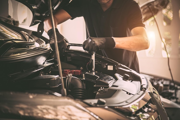 Meccanico automatico della mano del primo piano che utilizza la chiave per riparare il motore dell'auto