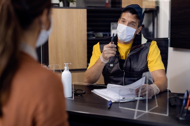 Meccanico automobilistico che parla con il suo cliente anche se la guardia per gli starnuti in ufficio durante la pandemia di coronavirus