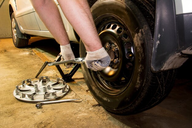 Meccanico che cambia la ruota dell'auto in garage. L'uomo lo scambio di pneumatici. Servizio pneumatici. Montaggio pneumatici.