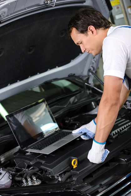 Meccanico che per mezzo di un computer portatile per controllare un motore di automobile.