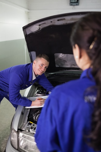 Meccanico che si appoggia su un&#39;auto mentre guardando un collega