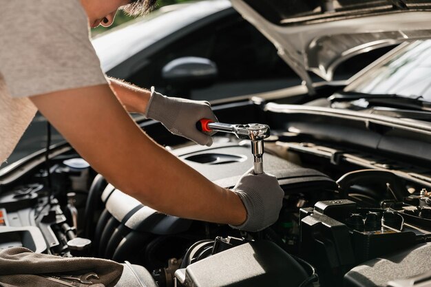 Meccanico che utilizza una chiave mentre lavora sul motore dell'auto presso l'officina del garage Manutenzione dei servizi automobilistici